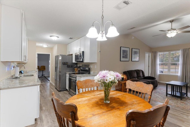 dining space featuring ceiling fan with notable chandelier, a textured ceiling, vaulted ceiling, sink, and light hardwood / wood-style flooring