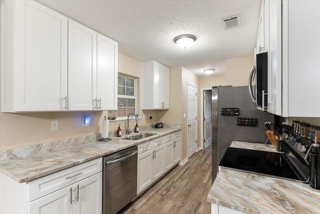 kitchen with white cabinetry, sink, light hardwood / wood-style floors, a textured ceiling, and appliances with stainless steel finishes