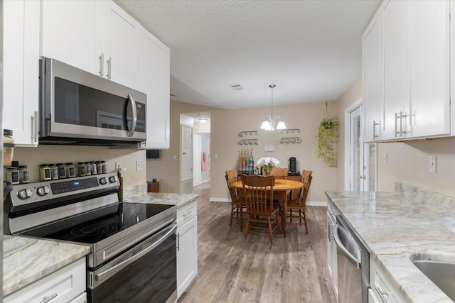 kitchen featuring an inviting chandelier, white cabinets, light stone countertops, a textured ceiling, and stainless steel appliances