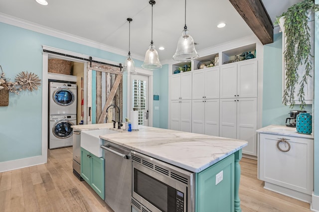 kitchen featuring stainless steel appliances, a kitchen island with sink, a barn door, stacked washer and clothes dryer, and hanging light fixtures