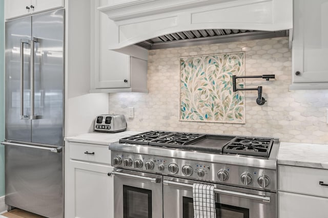 kitchen featuring high end appliances, decorative backsplash, custom range hood, light stone counters, and white cabinetry