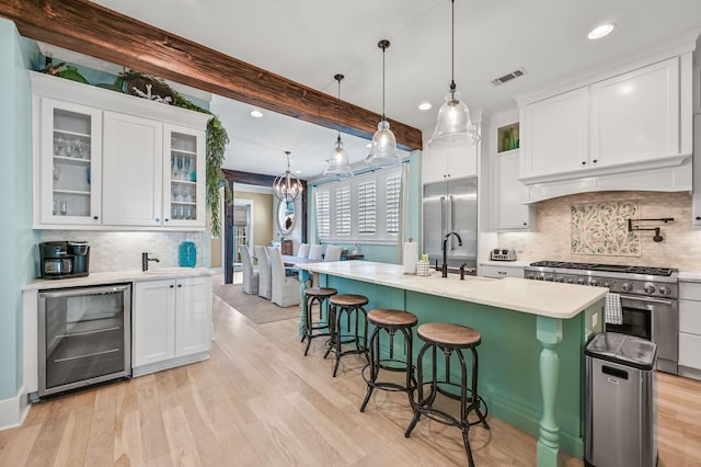 kitchen with white cabinets, premium appliances, a kitchen island with sink, beamed ceiling, and wine cooler