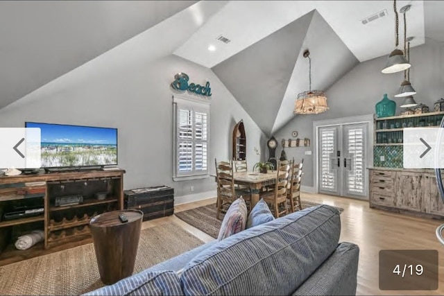 living room featuring french doors, a healthy amount of sunlight, lofted ceiling, and light wood-type flooring