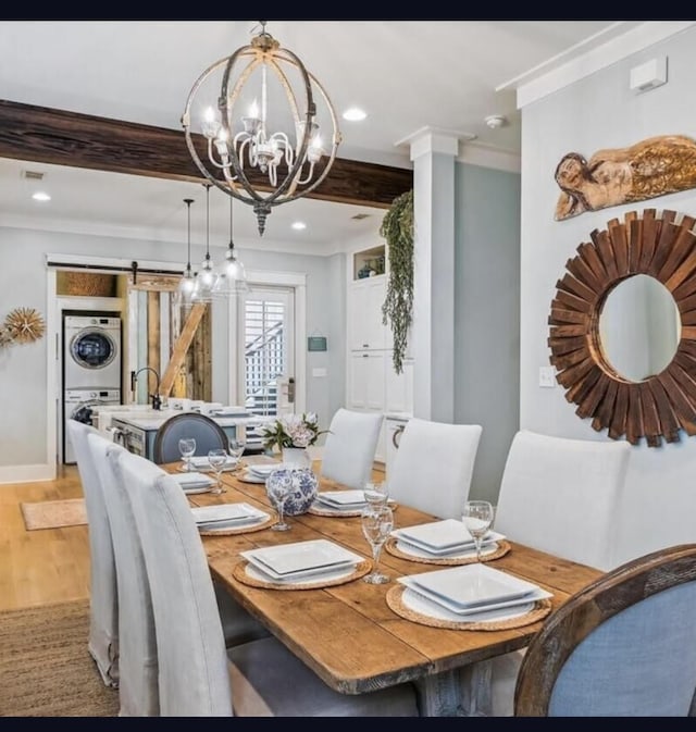 dining space featuring stacked washing maching and dryer, a barn door, a chandelier, wood-type flooring, and ornamental molding