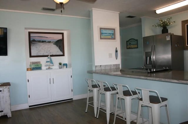 kitchen with dark hardwood / wood-style flooring, stainless steel refrigerator with ice dispenser, kitchen peninsula, crown molding, and a breakfast bar area