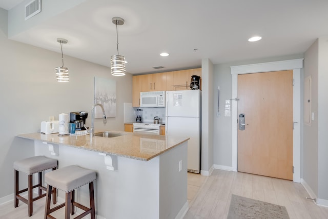 kitchen with sink, kitchen peninsula, decorative light fixtures, white appliances, and light brown cabinetry