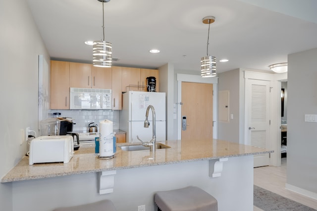 kitchen featuring light stone counters, light brown cabinetry, hanging light fixtures, and white appliances