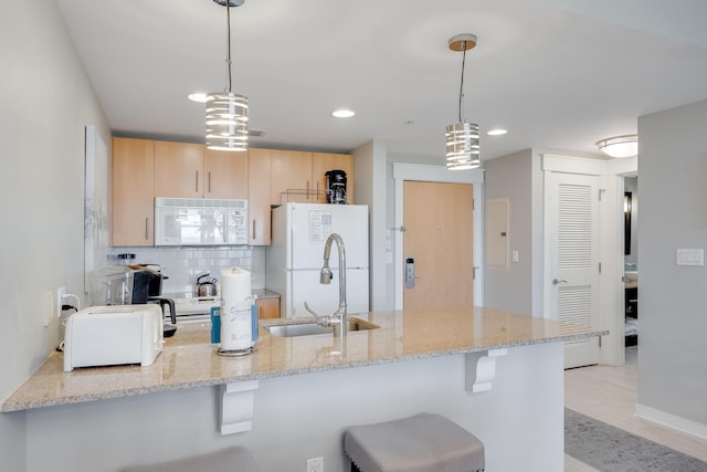 kitchen featuring white appliances, light stone countertops, light brown cabinetry, decorative light fixtures, and kitchen peninsula