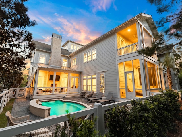 back house at dusk featuring a balcony, a fenced in pool, and a patio