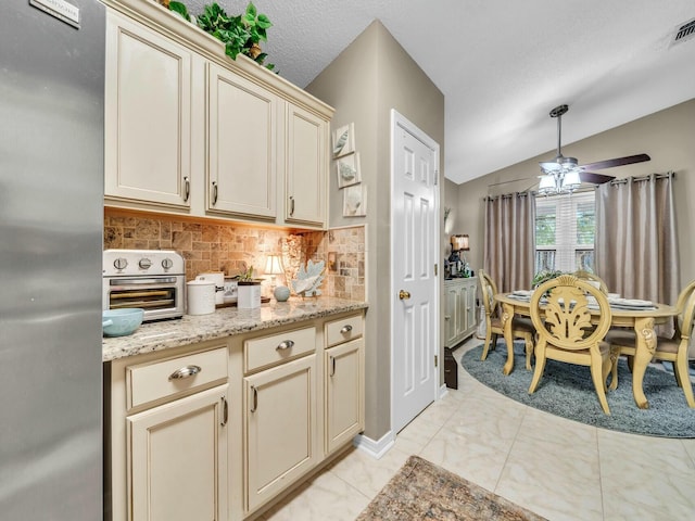 kitchen featuring decorative backsplash, vaulted ceiling, ceiling fan, cream cabinetry, and stainless steel refrigerator