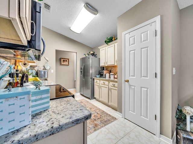 kitchen with stainless steel refrigerator with ice dispenser, tasteful backsplash, a textured ceiling, vaulted ceiling, and cream cabinets