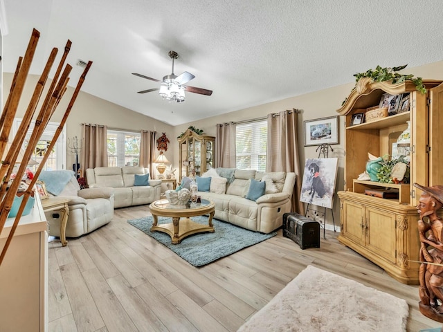 living room featuring ceiling fan, light hardwood / wood-style floors, lofted ceiling, and a textured ceiling