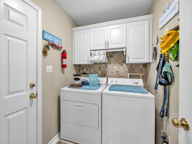 laundry room with washing machine and clothes dryer, cabinets, and a textured ceiling