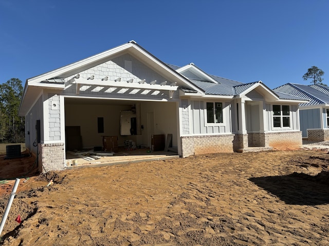 view of front of property with board and batten siding, metal roof, a garage, brick siding, and central AC unit