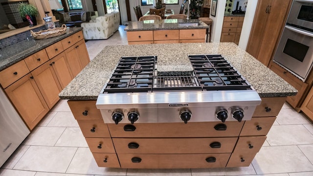 kitchen with light stone counters, a kitchen island, stainless steel appliances, and light tile patterned floors