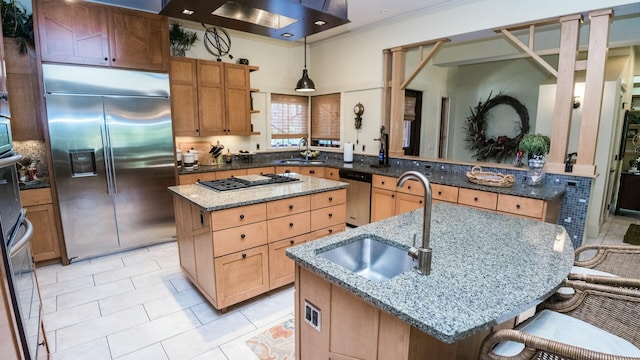 kitchen featuring appliances with stainless steel finishes, a center island with sink, stone counters, hanging light fixtures, and a breakfast bar area