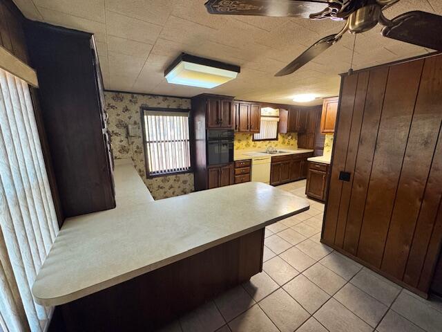 kitchen featuring kitchen peninsula, white dishwasher, ceiling fan, light tile patterned floors, and black oven