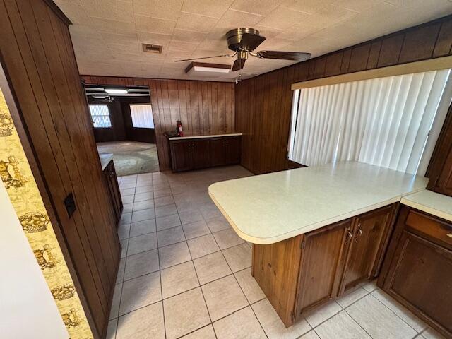 kitchen with kitchen peninsula, ceiling fan, light tile patterned floors, and wood walls