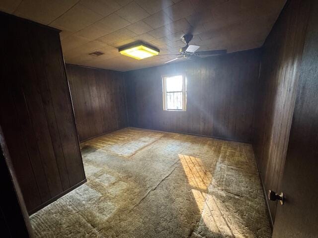 carpeted empty room with ceiling fan and wood walls