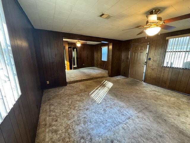 unfurnished room featuring carpet flooring, ceiling fan, and wood walls