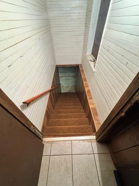 stairs with tile patterned flooring and wooden walls