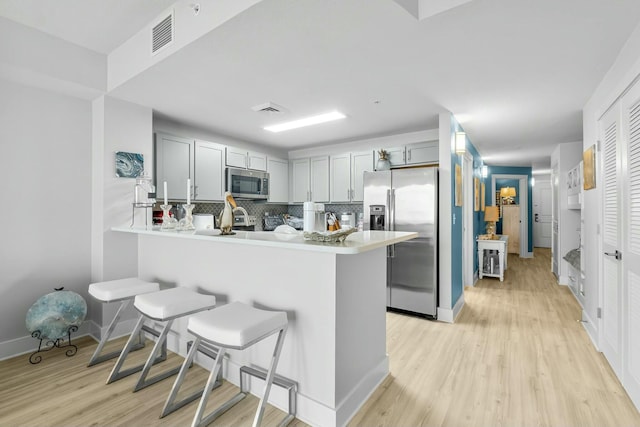 kitchen with kitchen peninsula, appliances with stainless steel finishes, decorative backsplash, and a kitchen breakfast bar