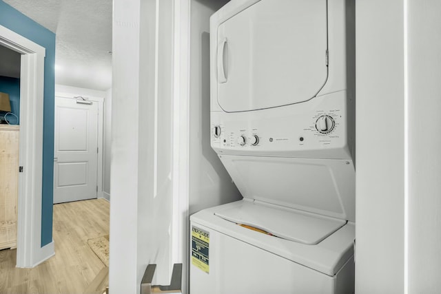 washroom featuring a textured ceiling, light hardwood / wood-style floors, and stacked washer / drying machine