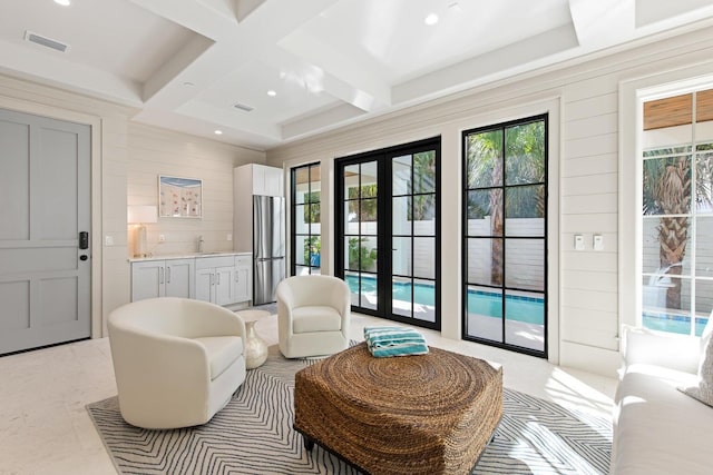 living area featuring beam ceiling, french doors, sink, coffered ceiling, and wooden walls