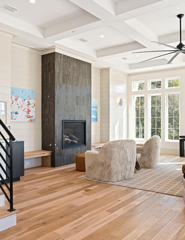 living room featuring ceiling fan, coffered ceiling, light hardwood / wood-style floors, wooden walls, and a fireplace