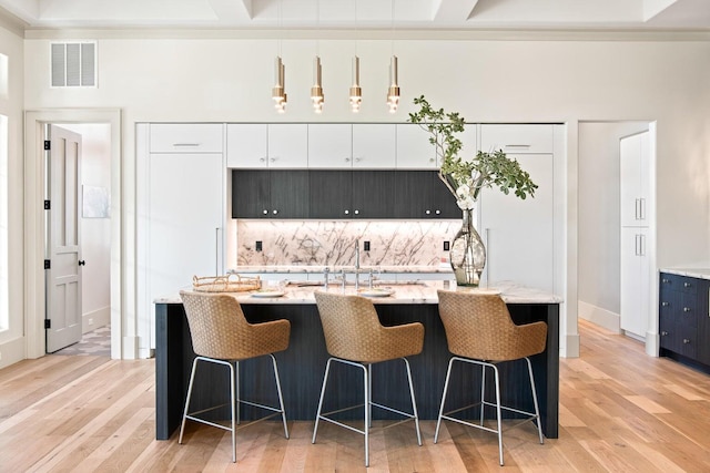 kitchen featuring decorative backsplash, light hardwood / wood-style flooring, white cabinets, and light stone counters