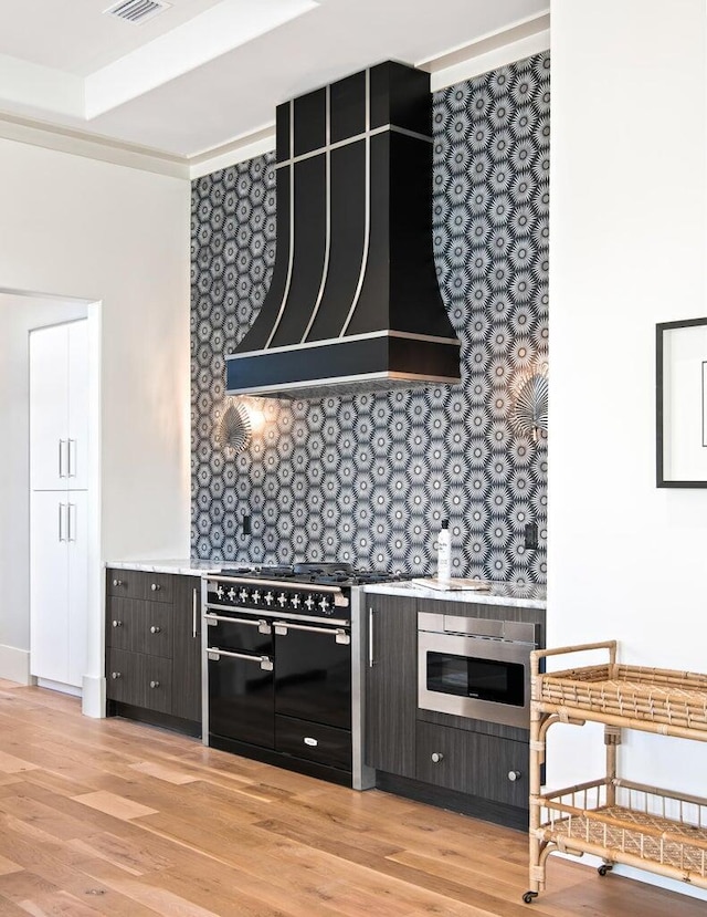 kitchen with tasteful backsplash, light hardwood / wood-style flooring, double oven range, and custom exhaust hood