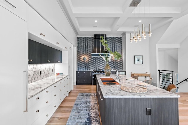 kitchen featuring light stone countertops, a center island with sink, white cabinets, and pendant lighting