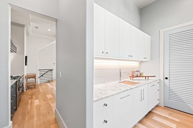 kitchen with white cabinets, light wood-type flooring, stainless steel gas range, and sink