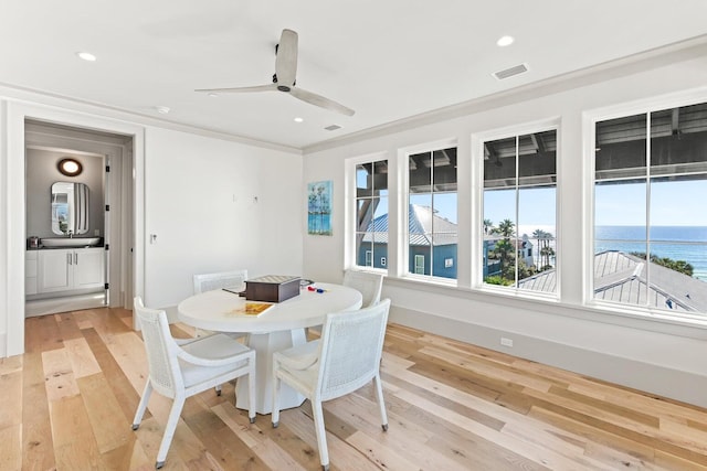 dining room with ceiling fan, light hardwood / wood-style floors, a water view, and crown molding