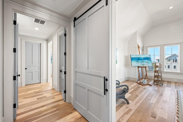 hallway with a barn door, light hardwood / wood-style flooring, and lofted ceiling