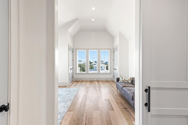 hall featuring light hardwood / wood-style floors, lofted ceiling, and wood walls