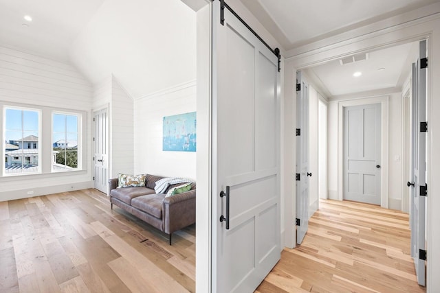 hallway with a barn door, light hardwood / wood-style flooring, and lofted ceiling