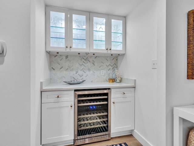 bar featuring white cabinets, light hardwood / wood-style flooring, beverage cooler, and backsplash