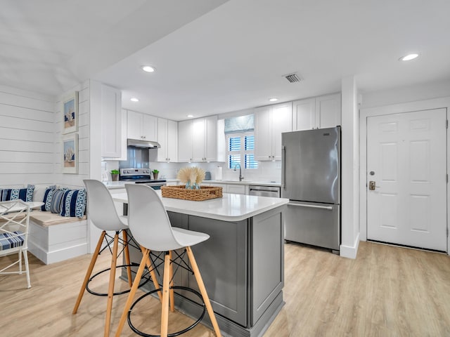 kitchen featuring a breakfast bar area, appliances with stainless steel finishes, light wood-type flooring, white cabinets, and sink