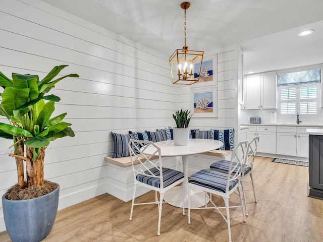 dining room with light wood-type flooring, an inviting chandelier, breakfast area, and wood walls