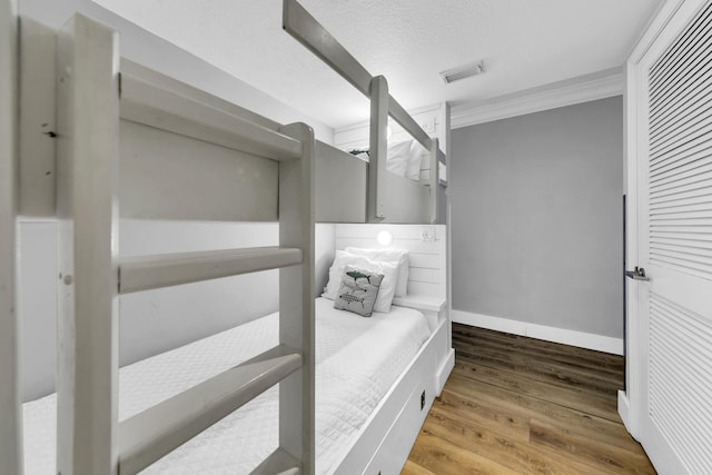 bedroom featuring wood-type flooring, crown molding, and a textured ceiling