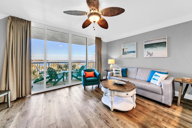 living room featuring ceiling fan, expansive windows, light wood-type flooring, and crown molding