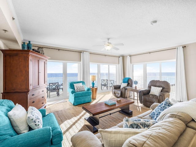 living room with ceiling fan, a water view, and a textured ceiling