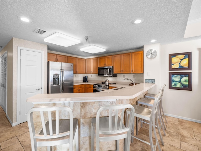 kitchen with sink, appliances with stainless steel finishes, a kitchen breakfast bar, a textured ceiling, and kitchen peninsula