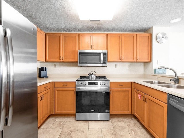 kitchen with a textured ceiling, light countertops, appliances with stainless steel finishes, and a sink