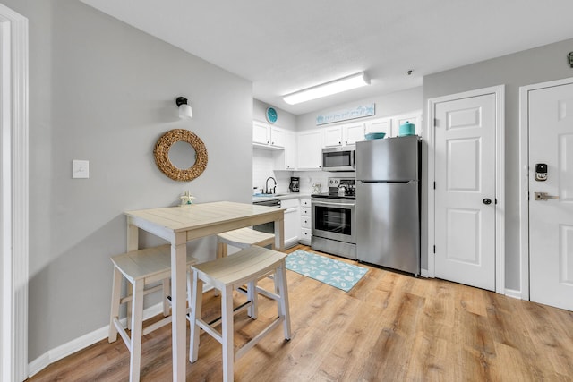 kitchen featuring backsplash, white cabinets, sink, light hardwood / wood-style floors, and stainless steel appliances