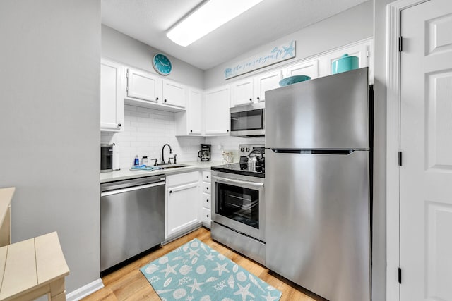 kitchen with white cabinets, appliances with stainless steel finishes, light hardwood / wood-style floors, and tasteful backsplash