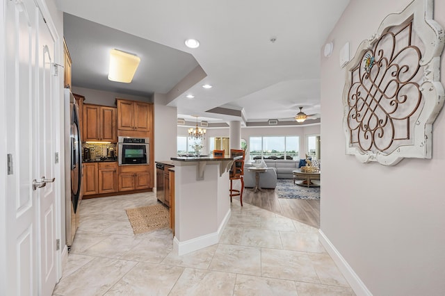 kitchen featuring a breakfast bar, ceiling fan with notable chandelier, an island with sink, stainless steel appliances, and beverage cooler