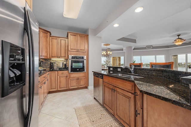 kitchen with ceiling fan with notable chandelier, sink, dark stone countertops, appliances with stainless steel finishes, and decorative light fixtures