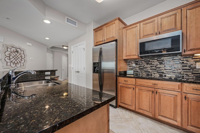 kitchen with backsplash, stainless steel appliances, sink, light tile patterned floors, and dark stone countertops